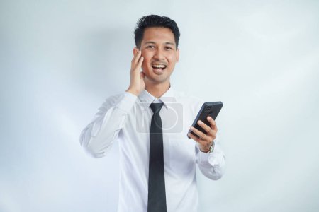 Photo for Adult Asian man showing surprised face expression when holding mobile phone - Royalty Free Image