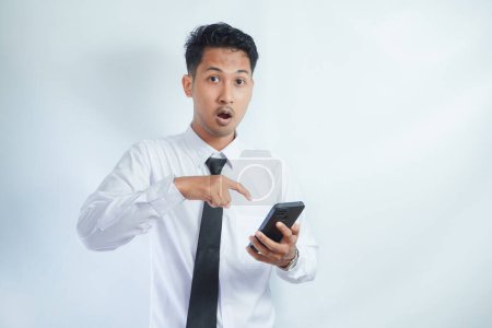 Photo for Adult Asian man pointing to mobile phone that he hold with wow expression - Royalty Free Image