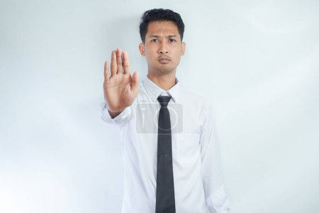 Adult Asian businessman looking camera and give stop hand sign with serious face expression