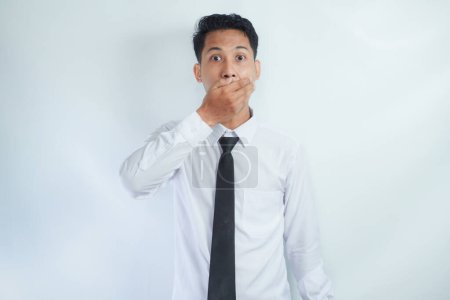 Kopfschuss eines verängstigten jungen asiatischen Geschäftsmannes, der den Mund bedeckt und mit verängstigtem Gesichtsausdruck in die Kamera schaut, aus Angst, bei der Arbeit gefeuert zu werden