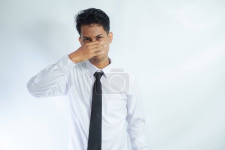 Asian businessman standing while covering his nose. Bad smell concept. Isolated on white