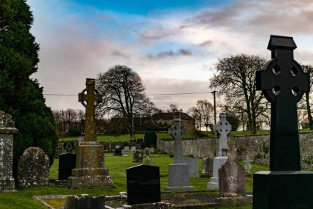 Foto de Cementerio sereno al atardecer con cruces celtas y lápidas contra un cielo dramático. - Imagen libre de derechos