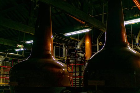 Foto de Fábrica de cerveza industrial alambiques de cobre y tanques de fermentación en un entorno oscuro con iluminación ambiental. - Imagen libre de derechos