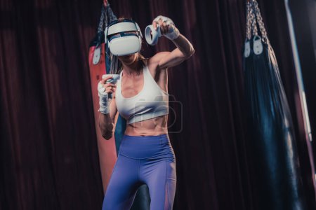 Photo for Fitness lovers battle against other gym members by wearing virtual reality goggles during intense boxing exercises. Learning and improving boxing techniques, from simple strikes to complex combos - Royalty Free Image