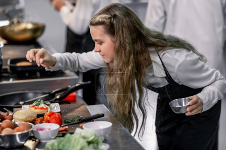 Téléchargez les photos : Les adolescents apprennent des chefs experts à l'école culinaire pour préparer des ingrédients et créer une variété de plats savoureux. Une activité pratique liée à leurs sens du goût et de l'odeur est de faire des hamburgers. - en image libre de droit