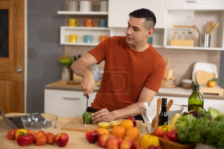 Photo for A homely and healthy male prepares nutritious diet, including variety of fruits. Following cooking show on laptop Mastery of peeling, chopping, and slicing fruits to prepare them in artistic style. - Royalty Free Image