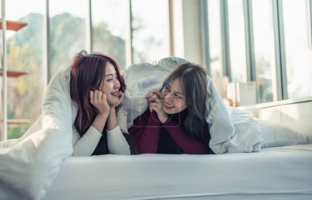 Photo for Asian lesbian couples are playing, smiling, relaxing, looking at each other under blanket in the bedroom. Every day, there are routine activities that need to be done at the beginning of the day. - Royalty Free Image
