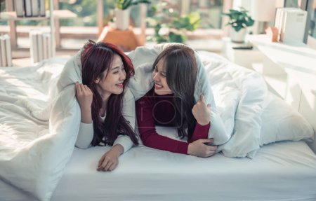 Téléchargez les photos : Les couples lesbiennes asiatiques jouent, sourient, se relaxent, se regardent sous la couverture dans la chambre. Chaque jour, il y a des activités de routine qui doivent être effectuées en début de journée.. - en image libre de droit