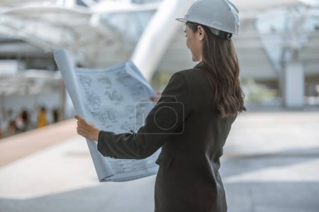 Photo for Skilled female architect meticulously inspects building site on and around Skytrain, cross referencing the blueprint and architectural layout. Implementing precise calculations for project approval. - Royalty Free Image