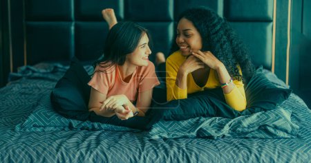 Foto de Amantes de las lesbianas participan en interacciones lúdicas en la cama. Sus ojos se encuentran con una mirada afectuosa, irradiando amor y ternura. Riendo, compartiendo momentos íntimos llenos de calidez y alegría. - Imagen libre de derechos
