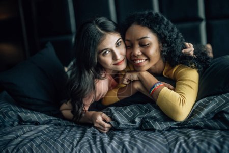 Foto de Las parejas lesbianas participan en momentos lúdicos en la cama acogedora, su risa llena el aire, creando un ambiente de alegría y afecto. Abrazan, comparten tiernos besos, mostrando felicidad genuina. - Imagen libre de derechos