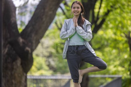 Photo for Young adult Asian female discovers revitalization through engaging in park yoga and meditation practices. Aligning physical, mental abilities Restoring energy levels, overall vitality, and well-being - Royalty Free Image