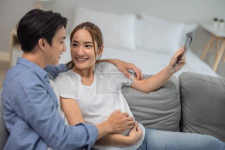 Foto de Las parejas asiáticas abrazan la alegría y la emoción del embarazo mientras escanean imágenes de ultrasonido, revelando la salud del bebé, el género y el desarrollo en el útero. La felicidad y la satisfacción fortalecen el vínculo familiar - Imagen libre de derechos