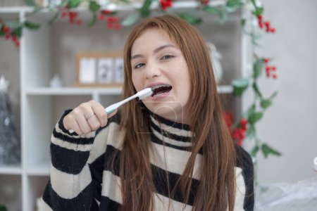 Photo for A mixed race teenage girl with dental braces smiles while holding a toothbrush in a festive decorated room. - Royalty Free Image