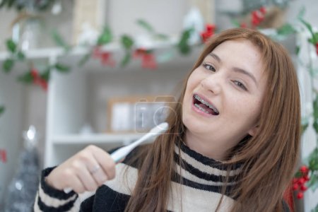 Téléchargez les photos : Une adolescente métisse avec des appareils dentaires sourit tout en tenant une brosse à dents dans une salle décorée festive. - en image libre de droit