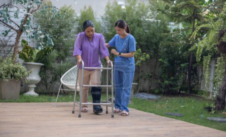 Photo for A caregiver attentively assists a patient using a walker during a rehabilitation walking exercise in a serene garden setting. - Royalty Free Image