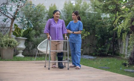 Téléchargez les photos : Un aidant aide attentivement un patient qui utilise une marchette lors d'un exercice de réadaptation dans un jardin serein.. - en image libre de droit