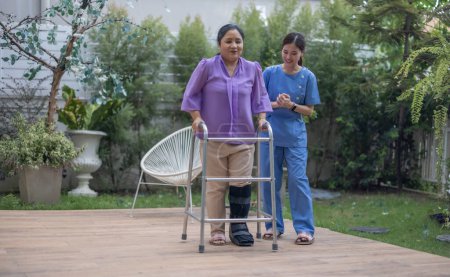 Eine Pflegekraft unterstützt einen Patienten während einer Reha-Gehübung in einer ruhigen Gartenlandschaft aufmerksam mit einem Rollator.
