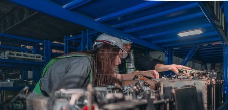 Foto de Dos ingenieros con cascos duros examinan piezas electrónicas en un almacén de componentes robóticos industriales por la noche. - Imagen libre de derechos