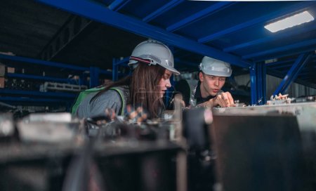 Photo for Two engineers with hard hats examine electronic parts in an industrial robotic component warehouse at night. - Royalty Free Image