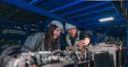 Téléchargez les photos : Deux ingénieurs munis de casques durs examinent des pièces électroniques dans un entrepôt de composants robotiques industriels la nuit. - en image libre de droit