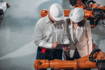 Photo for Senior engineer provides guidance to a trainee amidst robotic arms in a high-tech warehouse factory setting. - Royalty Free Image