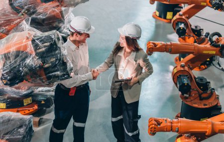 Téléchargez les photos : Un ingénieur principal guide un stagiaire au milieu de bras robotisés dans un entrepôt de haute technologie. - en image libre de droit