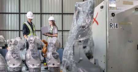 Foto de Ingeniero superior proporciona orientación a un aprendiz en medio de brazos robóticos en un entorno de fábrica de almacén de alta tecnología. - Imagen libre de derechos