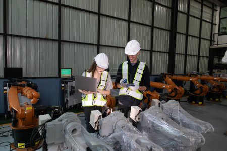 Senior engineer provides guidance to a trainee amidst robotic arms in a high-tech warehouse factory setting.