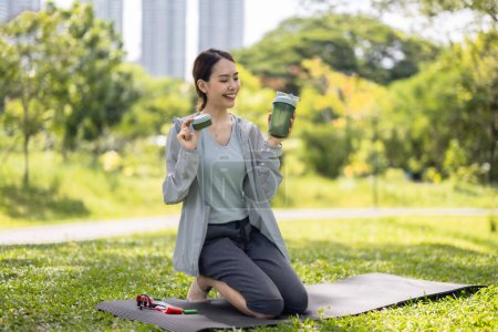 Téléchargez les photos : Une influenceuse des médias sociaux est capturée au milieu de la conversation, montrant une boisson protéinée en poudre à son public en ligne assis sur une pelouse verte luxuriante. - en image libre de droit