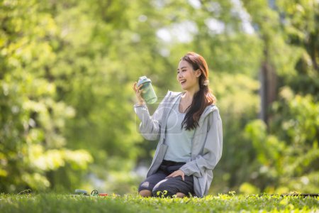 Foto de Una mujer influyente de las redes sociales es capturada a mitad de la conversación, mostrando una bebida de proteína en polvo a su audiencia en línea mientras está sentada en un exuberante césped verde. - Imagen libre de derechos