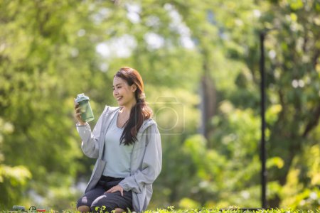Téléchargez les photos : Une influenceuse des médias sociaux est capturée au milieu de la conversation, montrant une boisson protéinée en poudre à son public en ligne assis sur une pelouse verte luxuriante. - en image libre de droit