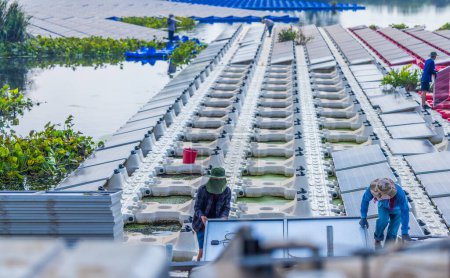Foto de Un equipo de trabajadores maniobra cuidadosamente un panel solar en su lugar entre filas de paneles en una gran granja solar flotante, mostrando energía renovable en acción. - Imagen libre de derechos