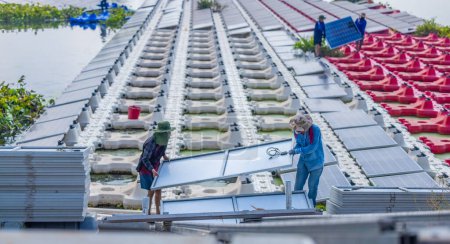 Téléchargez les photos : Une équipe de travailleurs manipule soigneusement un panneau solaire en place parmi des rangées de panneaux sur une vaste ferme solaire flottante, mettant en valeur les énergies renouvelables en action. - en image libre de droit