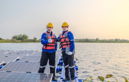 Foto de Dos técnicos están preparados y atentos en medio de una amplia gama de paneles solares en una granja solar flotante, a medida que la luz de la noche se desvanece en el fondo. - Imagen libre de derechos
