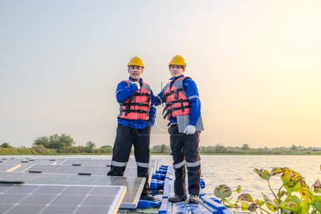 Téléchargez les photos : Deux techniciens se tiennent prêts et attentifs au milieu d'une vaste gamme de panneaux solaires sur une ferme solaire flottante, alors que la lumière du soir s'estompe en arrière-plan. - en image libre de droit