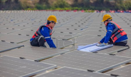 Foto de Dos ingenieros de cultivo solar están estudiando atentamente un conjunto de planos mientras realizan una inspección estándar de precisión entre filas de paneles fotovoltaicos. - Imagen libre de derechos
