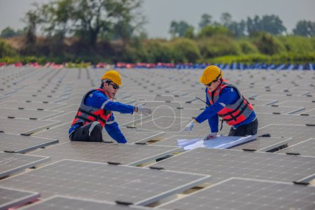 Foto de Dos ingenieros de cultivo solar están estudiando atentamente un conjunto de planos mientras realizan una inspección estándar de precisión entre filas de paneles fotovoltaicos. - Imagen libre de derechos