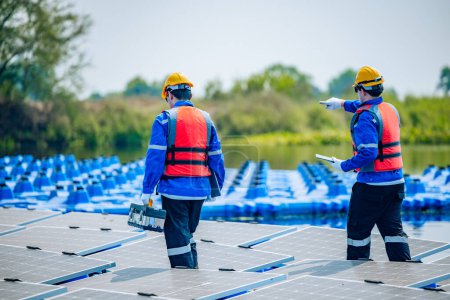 Foto de Dos ingenieros solares que usan equipo de protección y cascos inspeccionan visualmente las alineaciones, la estabilidad y la garantía de calidad de una gran variedad de paneles solares flotantes para cumplir con los requisitos estándar. - Imagen libre de derechos