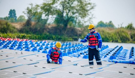Photo for Two solar engineers wearing protective gear and helmets visually inspect the alignments, stability, and quality assurance of a large array of floating solar panels to meet standard requirements. - Royalty Free Image