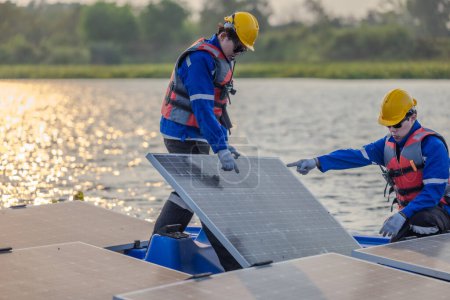 Photo for Two solar engineers wearing protective gear and helmets visually inspect the alignments, stability, and quality assurance of a large array of floating solar panels to meet standard requirements. - Royalty Free Image