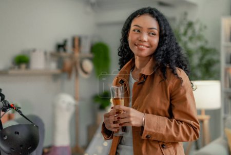 Eine junge, schwarze Startup-Designerin entspannt bei einem Glas Wein in einem einladenden Arbeitsbereich und reflektiert die Errungenschaften des Tages, umgeben von ihren lebendigen Kreationen.