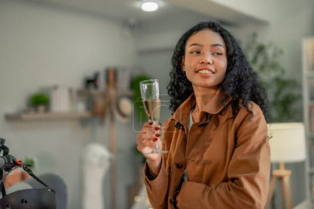 Téléchargez les photos : Une jeune créatrice de start-up noire se détend avec un verre de vin dans un espace de travail invitant, en réfléchissant sur les réalisations de la journée entourée de ses créations vives. - en image libre de droit