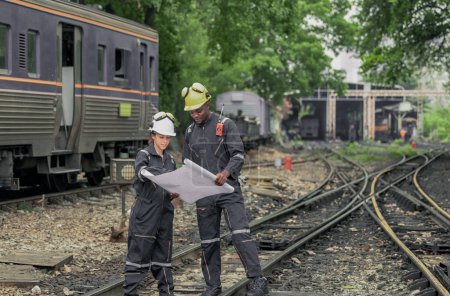 Foto de Los ingenieros de locomotoras colaboran y hacen referencia al plan para guiar la tarea de mantenimiento, solucionar problemas dentro de la infraestructura y la red rial. Garantizar la fiabilidad y la seguridad de las operaciones ferroviarias - Imagen libre de derechos
