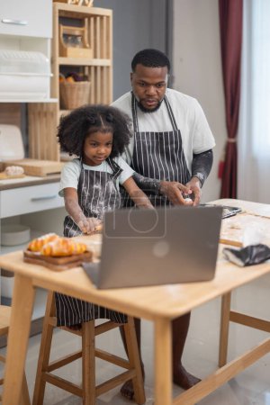 Photo for A family happily engages in baking together, using a laptop for guidance, surrounded by flour and bread rolls. - Royalty Free Image
