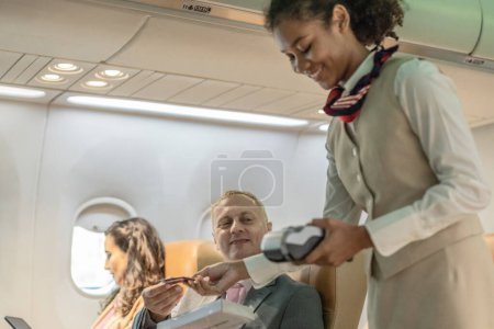 A female flight attendant assists business travelers with transactions during a flight.