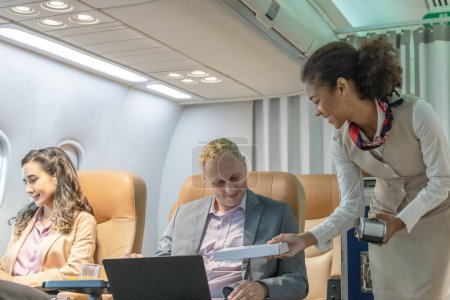Téléchargez les photos : Une hôtesse de l'air aide les voyageurs d'affaires à effectuer des transactions pendant un vol. - en image libre de droit