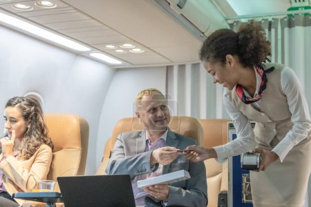 Téléchargez les photos : Une hôtesse de l'air aide les voyageurs d'affaires à effectuer des transactions pendant un vol. - en image libre de droit