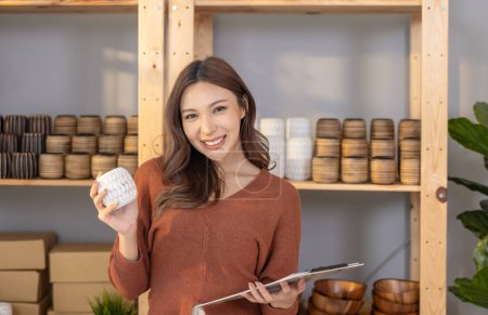 Téléchargez les photos : Des propriétaires d'entreprise confiants et souriants présentent des poteries artisanales dans un espace intérieur chaleureusement éclairé. - en image libre de droit