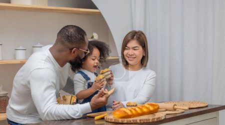 Téléchargez les photos : Une famille de trois personnes, avec un père, une mère et une fille, se délecte de la cuisson et du partage du pain à la maison. - en image libre de droit
